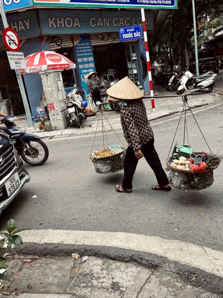 A street vendor in Hanoi's Old Quarter carries his goods using a traditional pole across his shoulders.