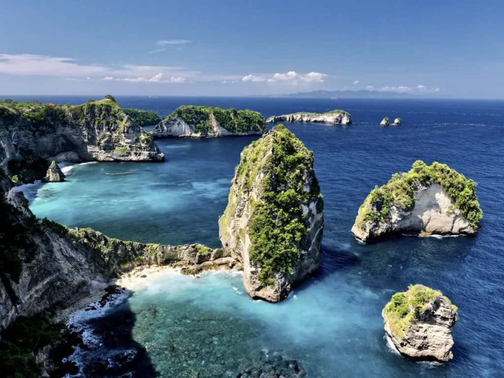 Diving Nusa Penida: The Full Guide to Mantas, Molas & Drifts 5 View from the sea of towering dark cliffs and lush greenery on Nusa Penida, with sparkling water in the foreground.