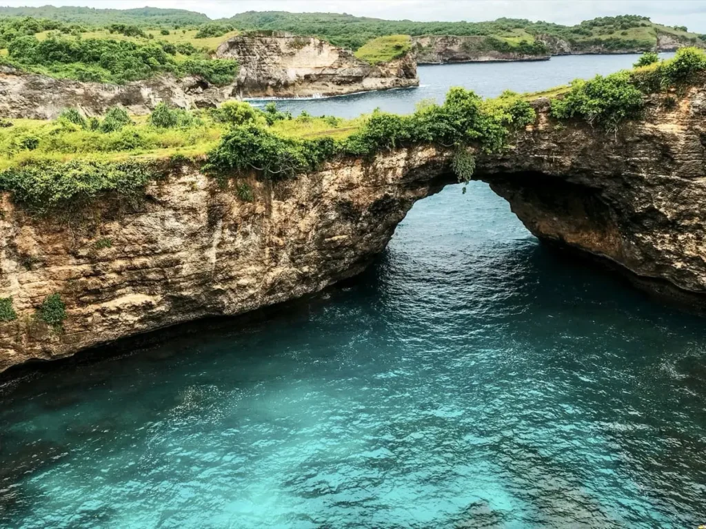 Diving Nusa Penida: The Full Guide to Mantas, Molas & Drifts 10 A wide natural rock bridge at Broken Beach on Nusa Penida with lush greenery above and clear turquoise water below