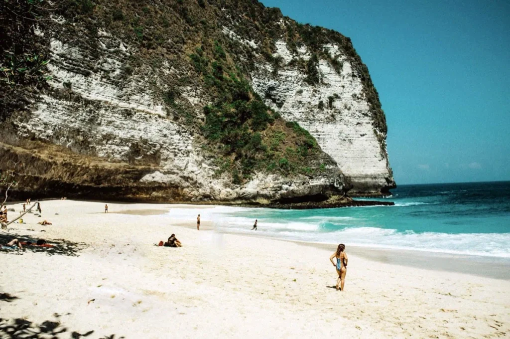 Diving Nusa Penida: The Full Guide to Mantas, Molas & Drifts 9 Tourists enjoy the golden sand and turquoise surf at Crystal Bay Beach, a popular diving and sunset spot on Nusa Penida.