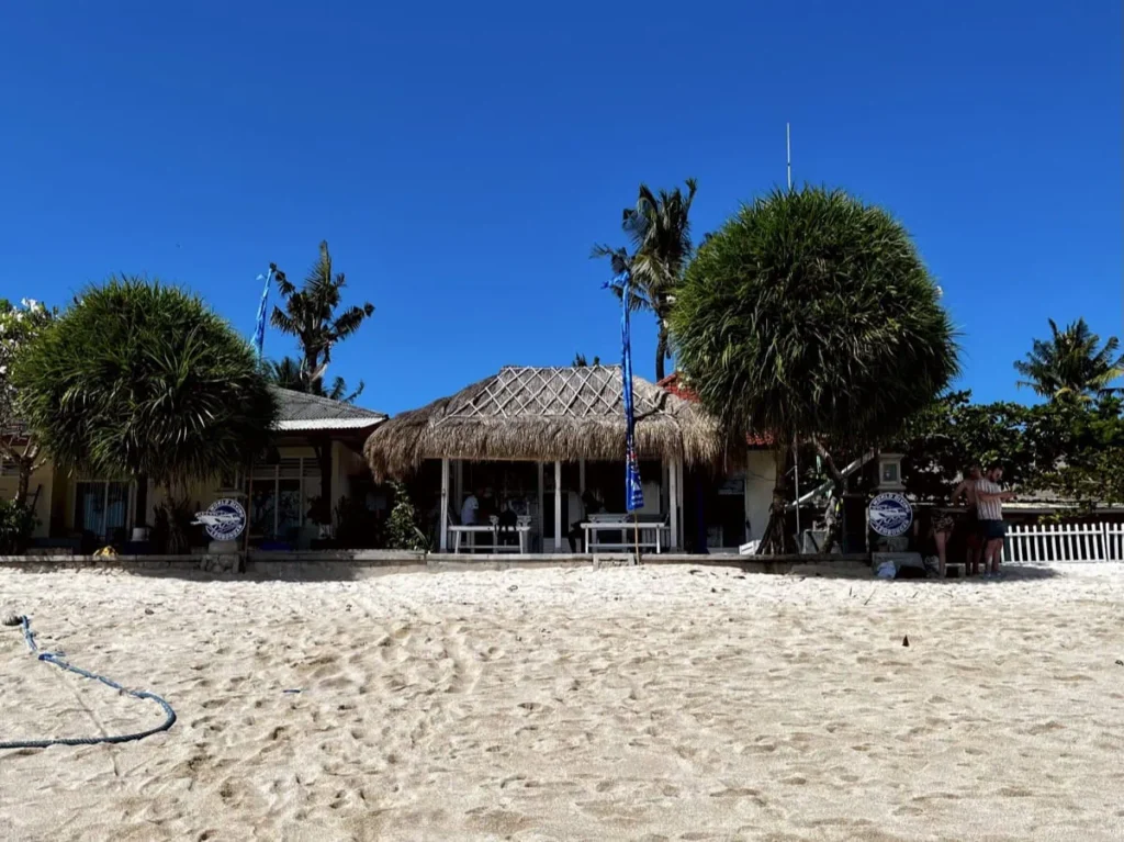 Diving Nusa Penida: The Full Guide to Mantas, Molas & Drifts 7 A beachside dive shop on Nusa Penida with palm trees and thatched roofs, a central hub for diving tours and gear rental.