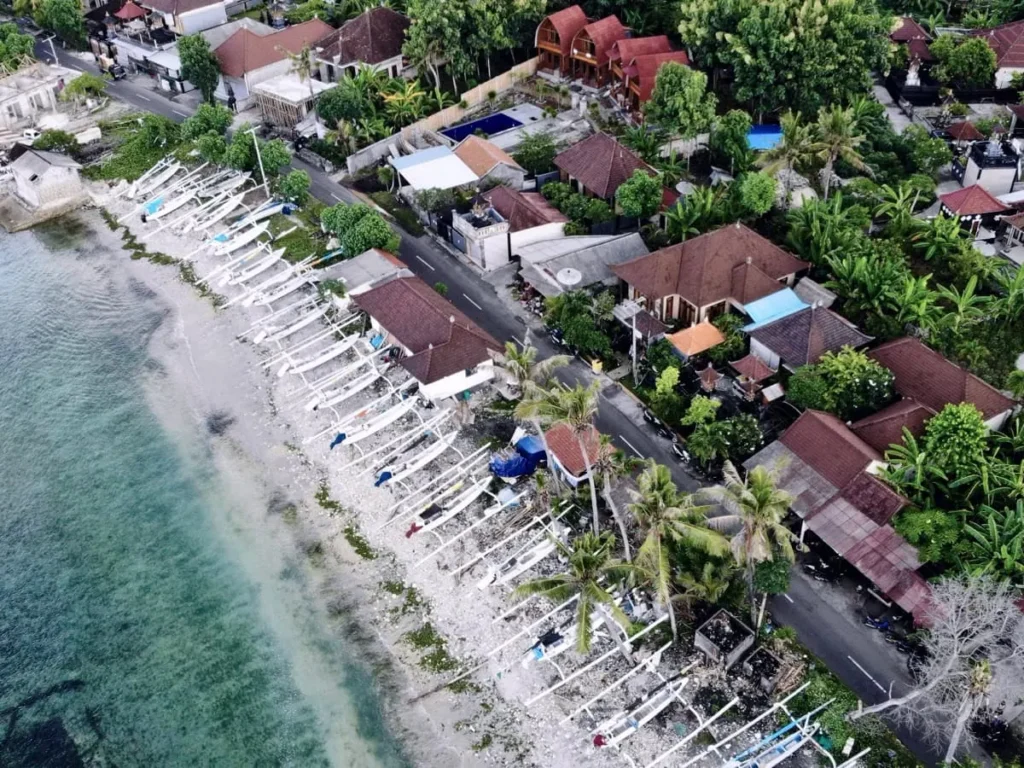 Aerial view of a coastal village in Nusa Penida with rows of traditional outrigger boats lined up along the shore.