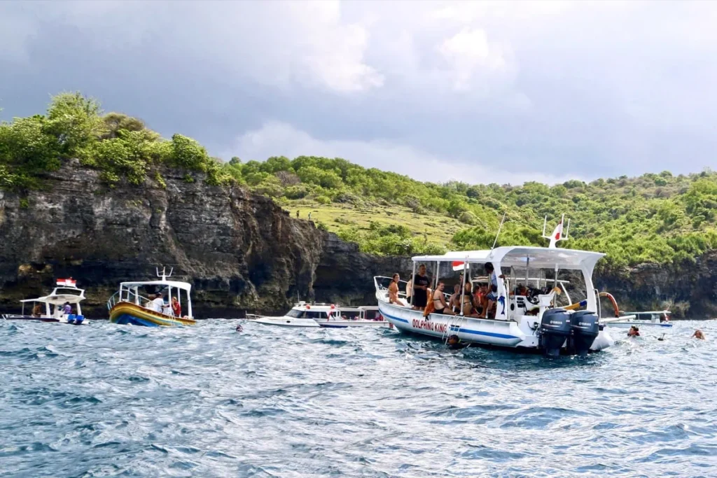 Best Snorkeling Spots in Nusa Penida + Safety Tips 8 A group of tourists prepares to snorkel from a boat near the lush coastline of Nusa Penida.