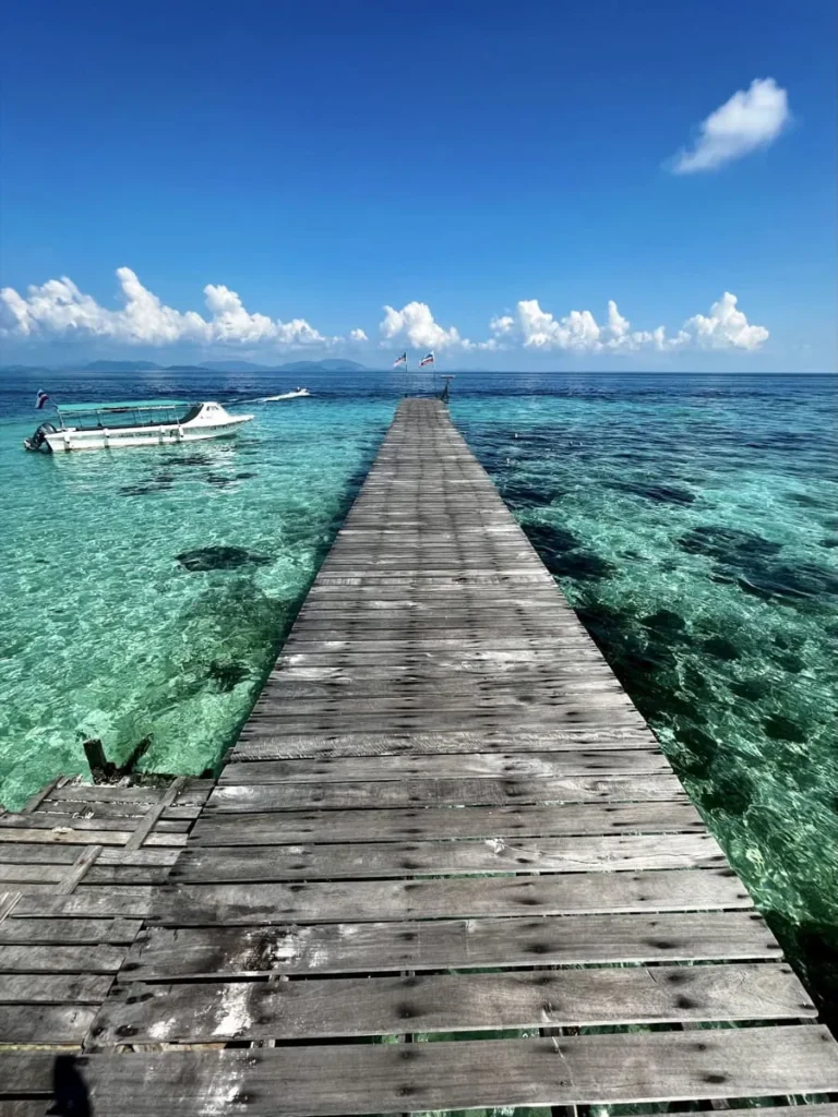 Long wooden pier stretching into clear blue sea with a speedboat moored beside it, capturing the journey out to dive sites around Sipadan.