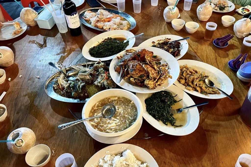 Table covered with seafood dishes including crab fish soup vegetables and rice during a meal in Semporna after diving. Plates and drinks are spread across the table showing typical food you can get for cheap when staying in Semporna town.