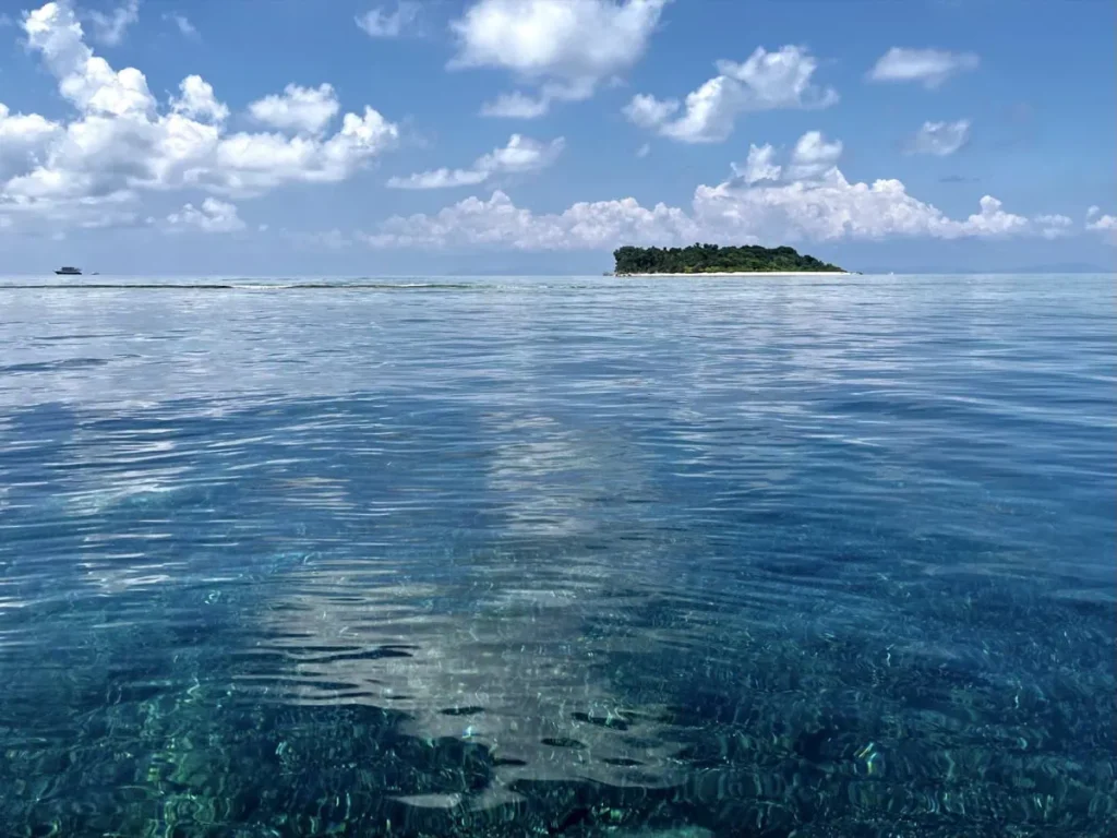 Calm turquoise sea stretching toward a small island on the horizon as seen from Kapalai, showing the remote setting of accommodation options near Sipadan.