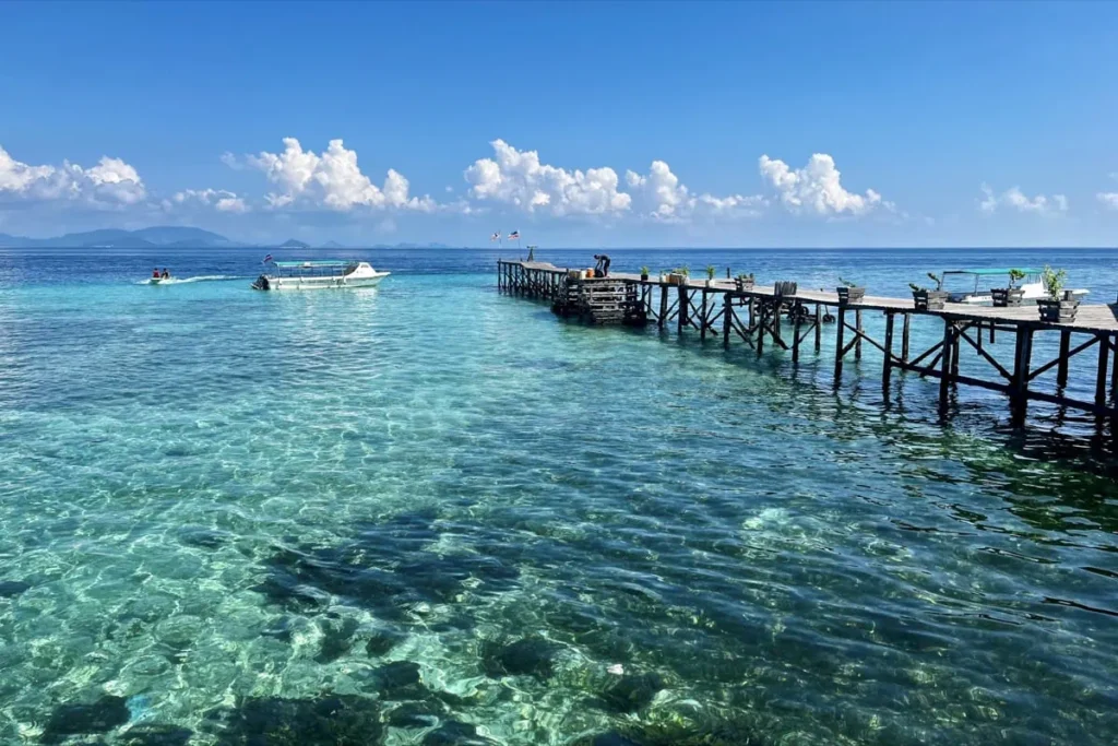 Wooden jetty on Mabul island stretching over clear turquoise water with a speedboat nearby where divers depart for day trips to Sipadan.